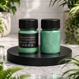 Two jars of bright green pigments on a black stand with plants in the background