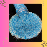 Blue glitter being poured from a bottle onto a black surface with a colorful border.
