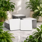 White and black striped cube-shaped ottomans on a marble floor with plants around.