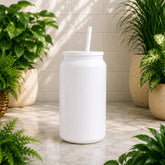 White tumbler with a straw on a light wooden surface surrounded by potted plants.