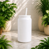 White tumbler with a straw on a light wooden surface surrounded by potted plants.
