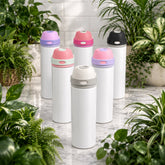 Set of white thermos bottles with colorful lids on a marble surface surrounded by plants