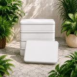 Stack of white containers on a stone surface with plants around