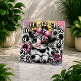 Decorative clock with a cow illustration and floral design on a stone surface.
