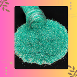 Turquoise glitter being poured from a bottle onto a black surface with a colorful border.