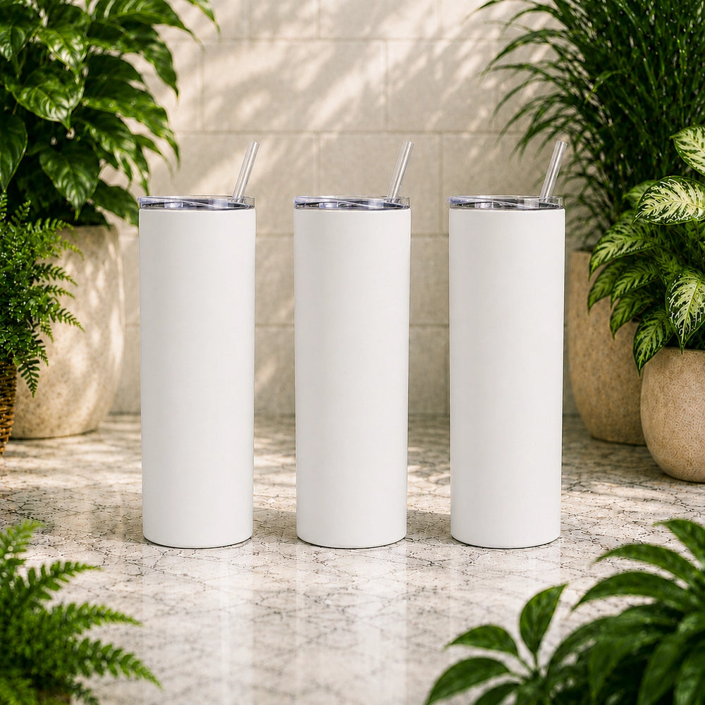 Three white tumblers with silver lids and straws on a stone surface with plants in the background.