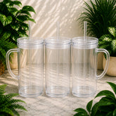 Three clear plastic tumblers with handles and straws on a stone surface with plants in the background.