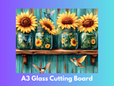 Decorative glass cutting board with sunflowers and jars on a wooden shelf against a blue wooden background.