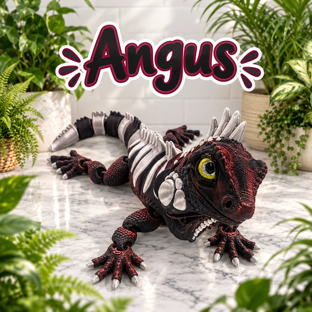 A realistic toy or model lizard/dinosaur-like creature with a red and black scaled body, white skeletal side details, a yellow eye, and large claws, posed on a marble surface with potted plants around it. The word 'Angus' appears prominently above the creature.
