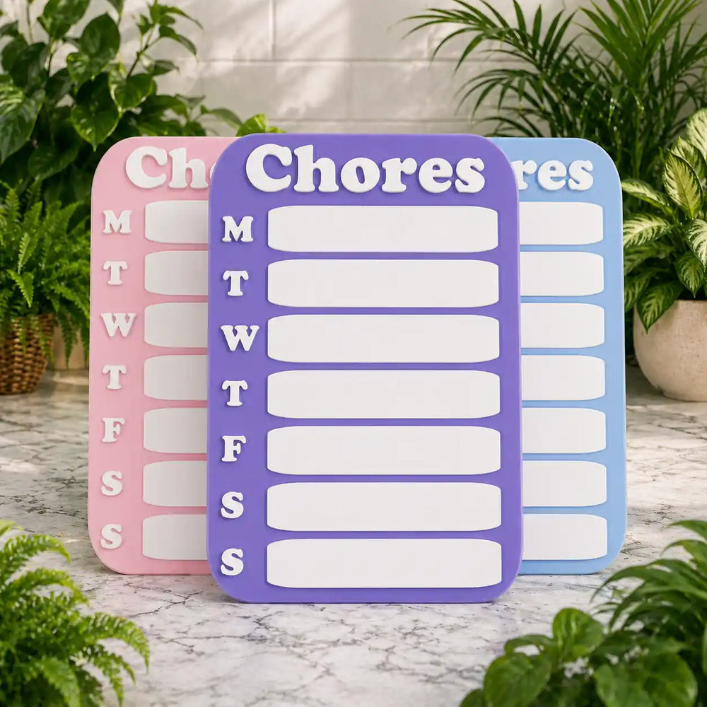 Three chore charts in pink, purple, and blue on a marble surface with plants in the background.
