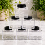 Stack of clear containers with black lids on a marble surface with plants in the background