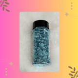 Bottle of blue glitter on a pink and yellow gradient background