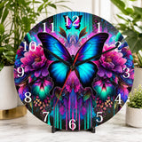 Decorative clock with a butterfly and floral design on a table with plants in the background.