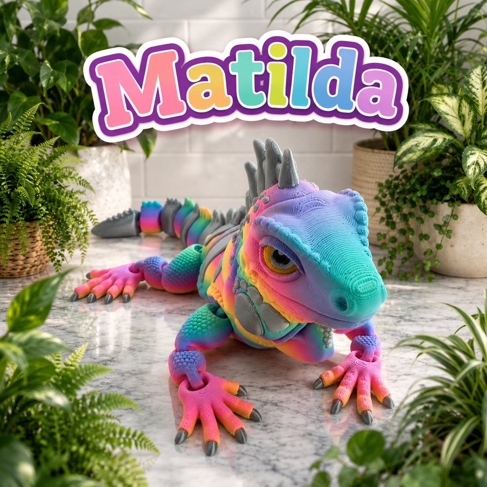 A colorful 3D-printed toy iguana labeled 'Matilda' in a stylized, cartoonish font at the top. The iguana features a vibrant rainbow gradient of purple, blue, green, yellow, and pink, with gray spikes on its back and pink claws.