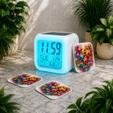 Digital clock with colorful butterfly design on a stone surface surrounded by plants