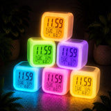 Stack of colorful digital alarm clocks on a dark surface with plants in the background.