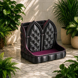 Black tufted cushion with purple interior on a stone floor surrounded by plants