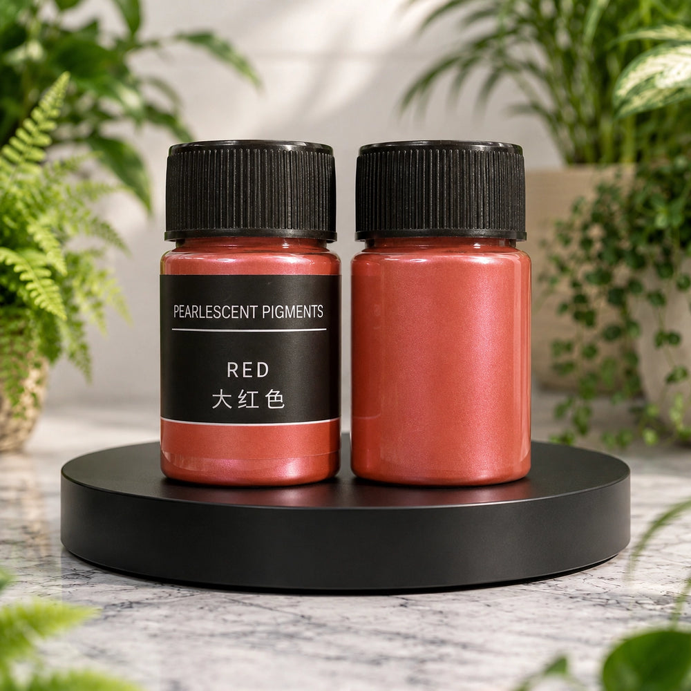 Two containers of red pearlized pigments on a black stand with green plants in the background.