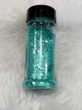 Turquoise glitter in a clear jar with a black lid on a white fur background