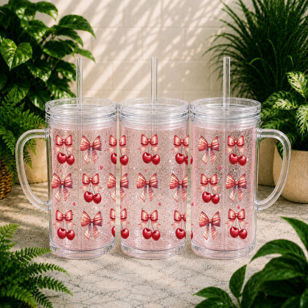 Three clear tumblers with red heart and pink bow pattern on a marble surface with plants in the background.