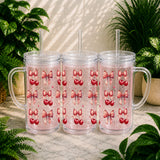 Three clear tumblers with red heart and pink bow pattern on a marble surface with plants in the background.